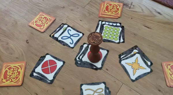 Karty gry Jungle Speed rozłożone na podłodze, gotowe do szybkiej rozgrywki. Drewniany totem pośrodku.