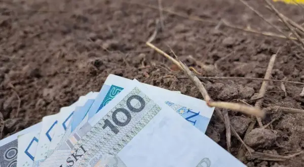 Pieniądze leżą na ziemi, symbolizując trud rolnika i jego ubezpieczenie społeczne.
