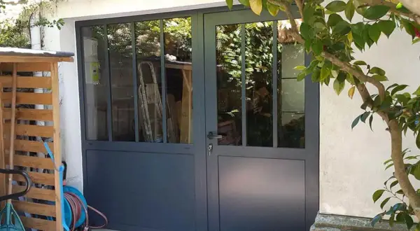 Remplacer porte de garage par fenêtre : une nouvelle entrée lumineuse avec des portes vitrées grises. Des outils de jardin sont rangés à gauche.