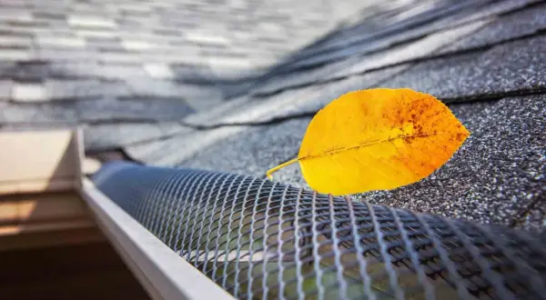 A yellow leaf rests on a newly installed gutter guard, showcasing its effectiveness against falling debris.