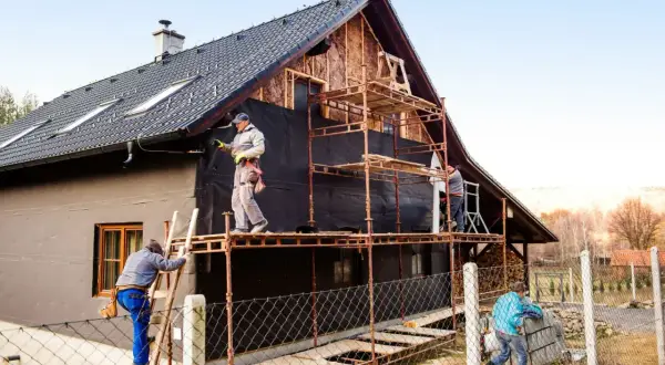 Pracownicy na rusztowaniach ocieplają dom. Określenie ceny ocieplenia za 1m2 robocizna wymaga analizy.