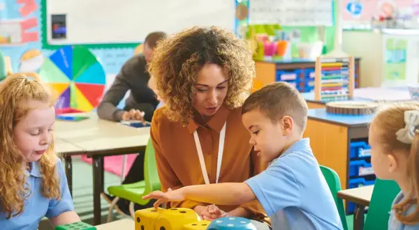 Lehrerin erklärt Kindern in der Schule Mathe mit Würfeln.