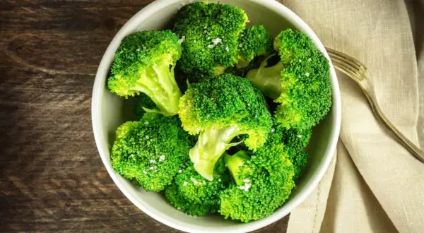En skål med nykokt, grön broccoli, strödd med flingsalt. En gaffel ligger bredvid på en beige duk.