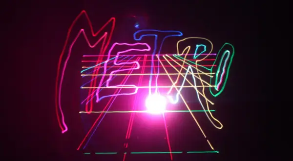 Kolorowe, neonowe linie tworzą napis "METRO" na czarnym tle, przypominając o energetycznym, musical metro.