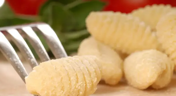 Une fourchette pique un gnocchi fait maison, prêt pour une délicieuse recette gnocchi. Des gnocchis frais et des ingrédients italiens en arrière-plan.