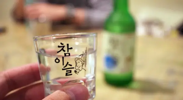Szklaneczka z soju, na której widnieje napis "참이슬" i rysunek. Zastanawiasz się, soju ile procent?