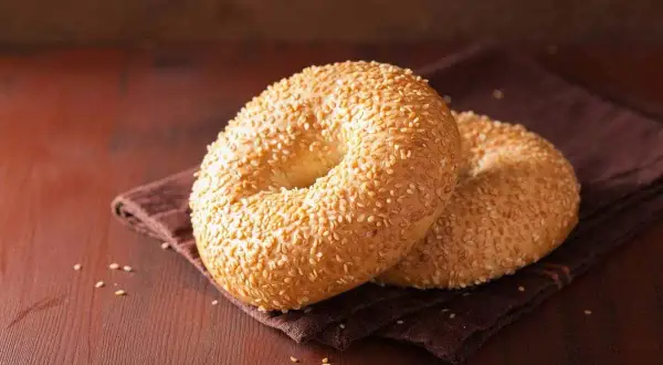 Deux bagels dorés, recouverts de graines de sésame, sur une serviette brune. Parfait pour une recette bagel moelleux.