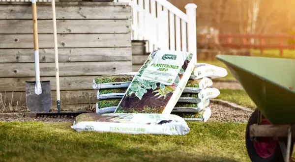 Säckar med planteringsjord, en spade och en kratta står redo för trädgårdsarbetet. Den kalkrika jorden är perfekt för att ge dina växter en bra start.