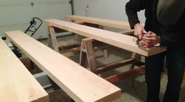 Man sanding Douglas fir planks on sawhorses, preparing them for staining.