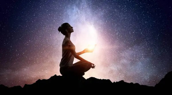 Silueta de mujer meditando bajo un cielo estrellado, sosteniendo una luz brillante. Conexión cuantica espiritual.