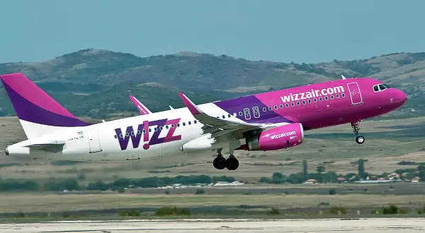 Dwa samoloty Wizz Air z różowymi i fioletowymi elementami startują na tle wzgórz.