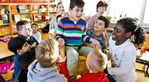 Kinder umringen einen Jungen im Stuhl. Ein lebendiges Bild vom **Unterricht Grundschule**, wo Lernen Spaß macht.