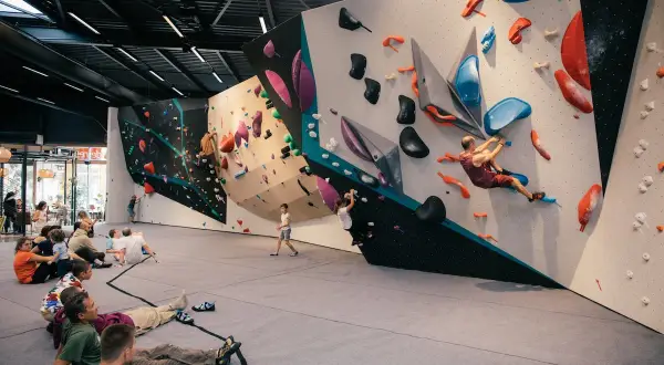 Des personnes se reposent au sol pendant que d'autres commencent l'escalade sur des murs colorés et texturés.