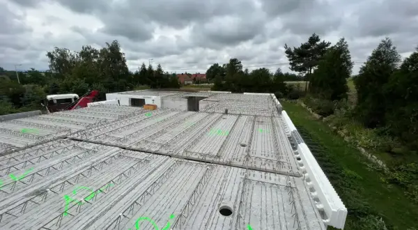 Gotowy do zalania strop żelbetowy, zbrojenie czeka na beton. W tle drzewa i pochmurne niebo.