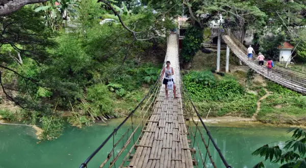 Młody mężczyzna idzie przez bambusowy most wiszący nad turkusową rzeką na Bohol, Filipiny.