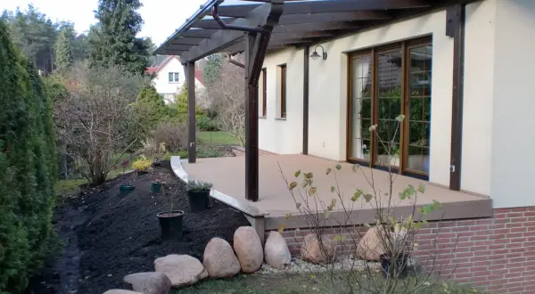 Terrasse sanieren: Neue Holzterrasse mit Überdachung, daneben frisch aufgeschüttete Erde und Steine für die Gartengestaltung.