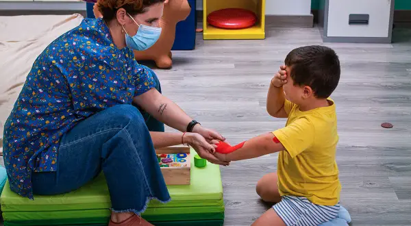 Niña recibe terapia ocupacional infantil, con un terapeuta aplicando pintura roja en su brazo.