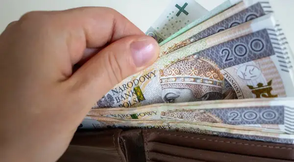 Dłoń wkłada polskie banknoty 200 zł do portfela. Zastanawiasz się, ile wynosi składka zdrowotna?