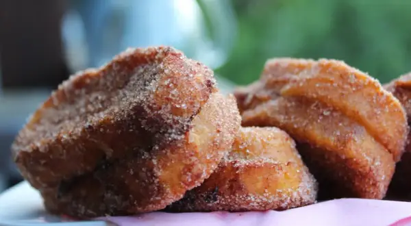 Süße Zwetschgen Bavesen, goldbraun frittiert und in Zimt-Zucker gewälzt, liegen auf einem rosa Tuch.