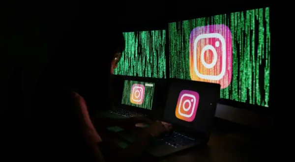 Osoba pracuje przy komputerze, na ekranach widnieje logo Instagrama i zielony kod. Szuka informacji, jak odzyskać zhakowane konto na Instagramie.