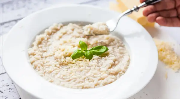 Kremowe risotto z parmezanem i bazylią na białym talerzu, widok z góry.