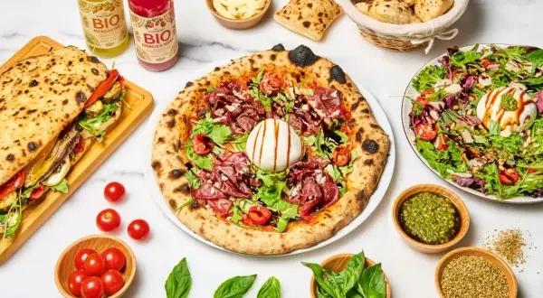 Une pizza diavola appétissante, garnie de charcuterie, burrata et roquette, accompagnée d'un sandwich, de salade et de boissons bio.