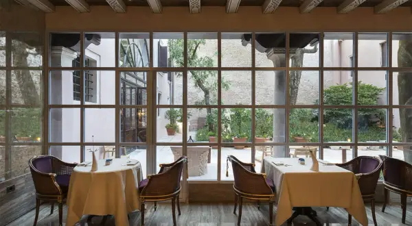 Tavoli apparecchiati in un elegante ristorante stellato Veneto, con vista su un cortile interno.