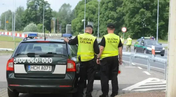 Funkcjonariusze Służby Celno-Skarbowej w kamizelkach odblaskowych przy radiowozie. Zarobki w tej służbie są adekwatne do odpowiedzialności.