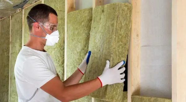 Operaio con mascherina e occhiali installa pannelli di lana di roccia per un cappotto termoisolante.