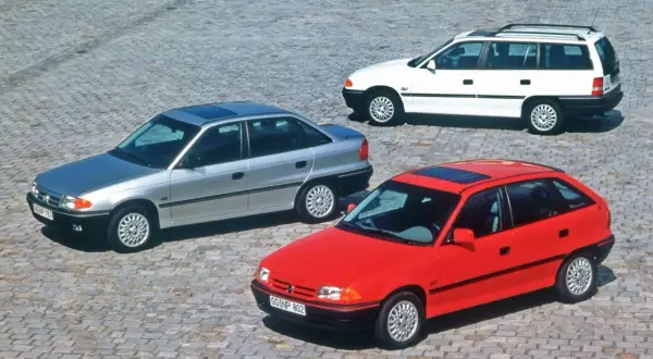 Trzy Ople Astra F: czerwony hatchback, srebrny sedan i białe kombi. Wśród nich wyróżnia się sportowy Opel Astra F GSI.