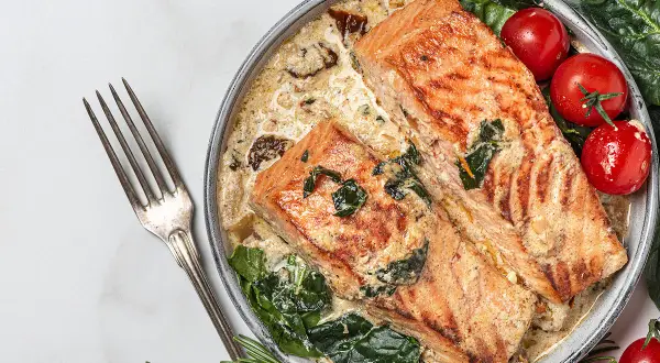 Deux pavés de saumon grillé dans une sauce crémeuse aux épinards, accompagnés de tomates cerises. Une recette saumon parfaite pour un dîner savoureux.