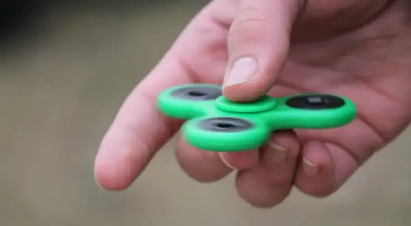 Groene fidget spinner in hand, een hulpmiddel voor concentratie bij hoog functionerend autisme.