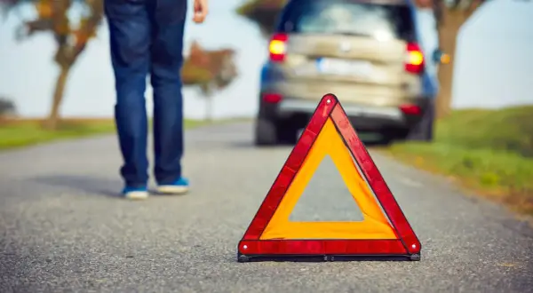 Triángulo de emergencia en carretera. Persona se aleja de coche averiado, lista para proteger, alertar y socorrer.