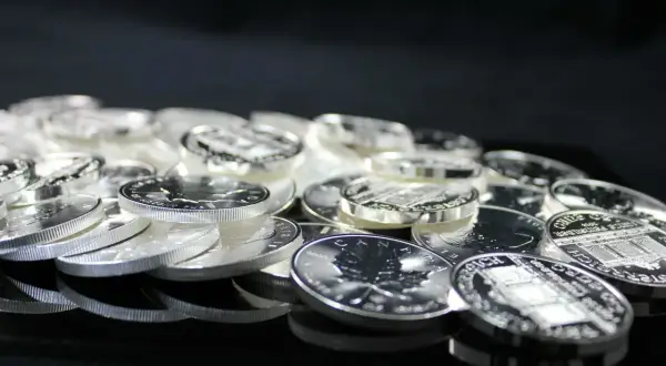 Stos monet ze srebra, błyszczące w świetle. Widać na nich detale, jak liść klonu i budynki. To inwestycja, która może być opodatkowana, czyli vat na srebro.