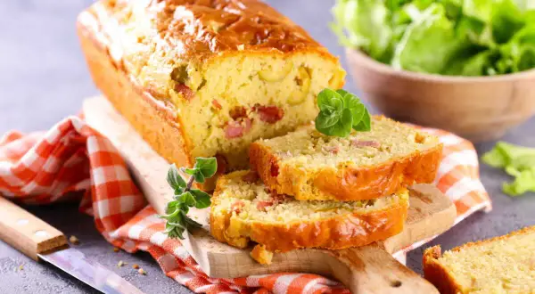 Un cake chorizo poivron, doré et moelleux, coupé en tranches sur une planche en bois. Une salade verte est servie à côté.