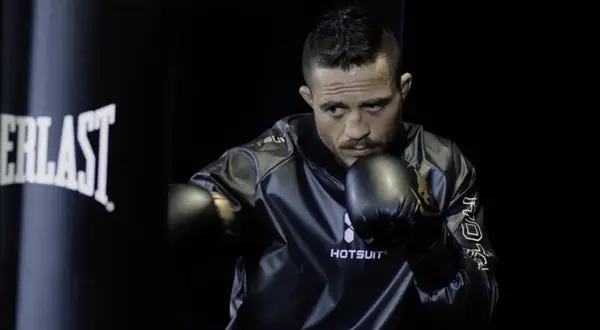 A determined boxer, wearing black gloves and a shiny jacket, practices ghost boxing in front of a dark Everlast punching bag.