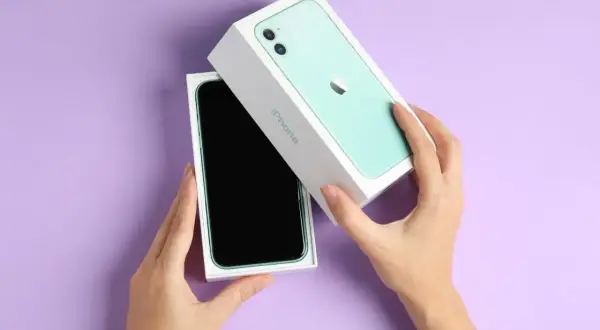Ręce rozpakowują zielony iPhone 11. Aparat tego modelu pozwala uchwycić każdy piksel z niezwykłą precyzją.