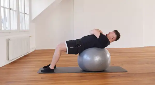 Un homme effectue un exercice avec ballon, le dos courbé sur le ballon de gym, les mains croisées sur la poitrine.