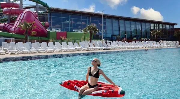 Frau entspannt auf aufblasbarem Kissen im Pool des Aquaparks Breslau, im Hintergrund Wasserrutschen und Liegestühle.