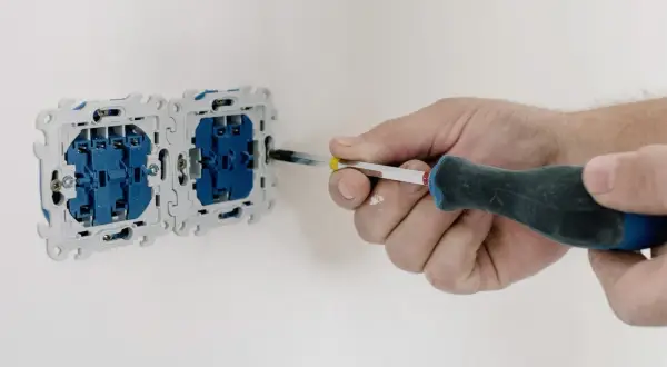 Elektryk dokręca śrubę w gniazdku elektrycznym, przygotowując je do pomiaru rezystancji izolacji.