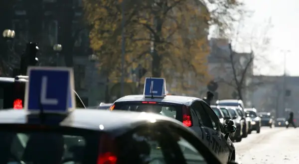 Samochody nauki jazdy z literą "L" na dachu stoją w korku ulicznym.