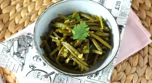 Un tazón de judías verdes salteadas con ajo y perejil, servido sobre un mantel de mimbre.