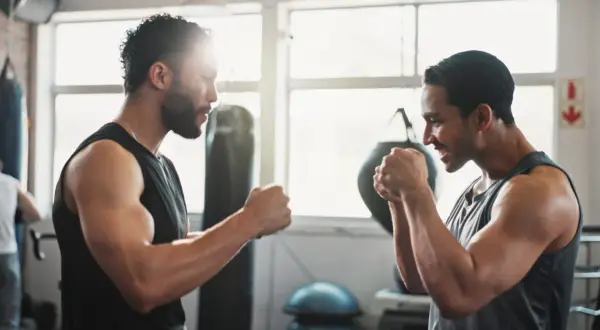 Two men spar in a gym, channeling the intensity of a Rocky Marciano workout. Punching bags and bright windows frame their focused faces.