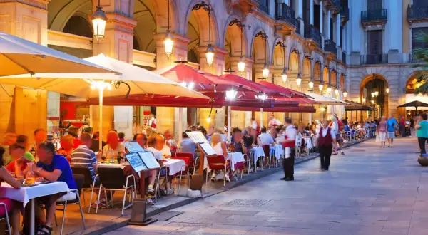 Kvällssol över många uteserveringar med folk som äter och dricker. En livlig atmosfär på restauranger i Barcelona.