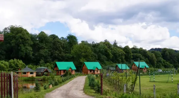 Gospodarstwo Jabłonica Ruska: malownicze drewniane domki z zielonymi dachami, staw, las i boisko.