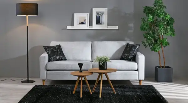 Grå soffa med svarta marmorkuddar, två runda träbord, svart matta och golvlampa i modern stil.