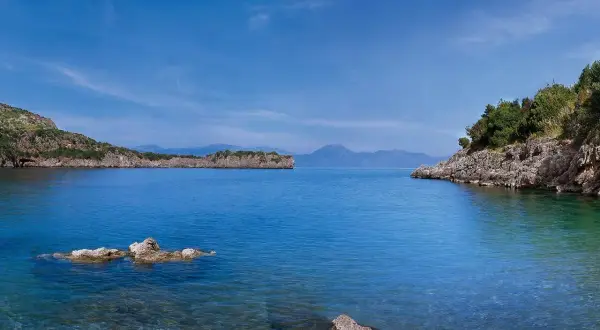 Calmo mare a maggio, con scogli affioranti e coste verdi sotto un cielo azzurro.