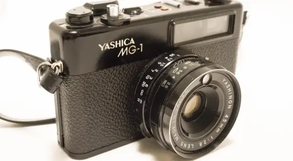 A black Yashica MG-1 camera with a leather strap. The lens reads "YASHINON 45mm 1:2.8".