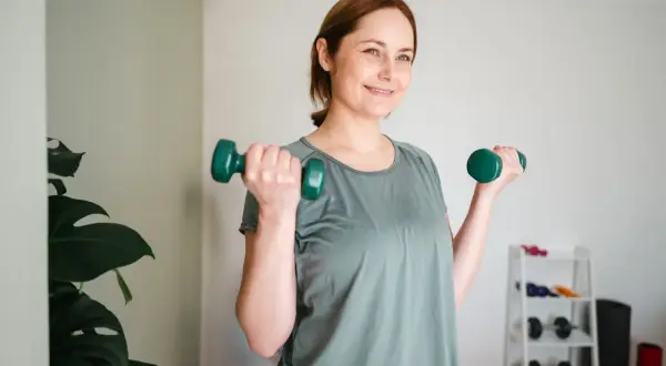 Lächelnde Frau macht Krafttraining mit Hanteln. Sie ist auf dem Weg zum Abnehmen und fühlt sich gut.