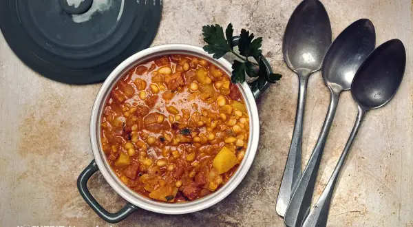 Herzhaftes Bohneneintopf Rezept mit Speck und Kartoffeln, garniert mit Petersilie. Daneben liegen drei Löffel bereit.